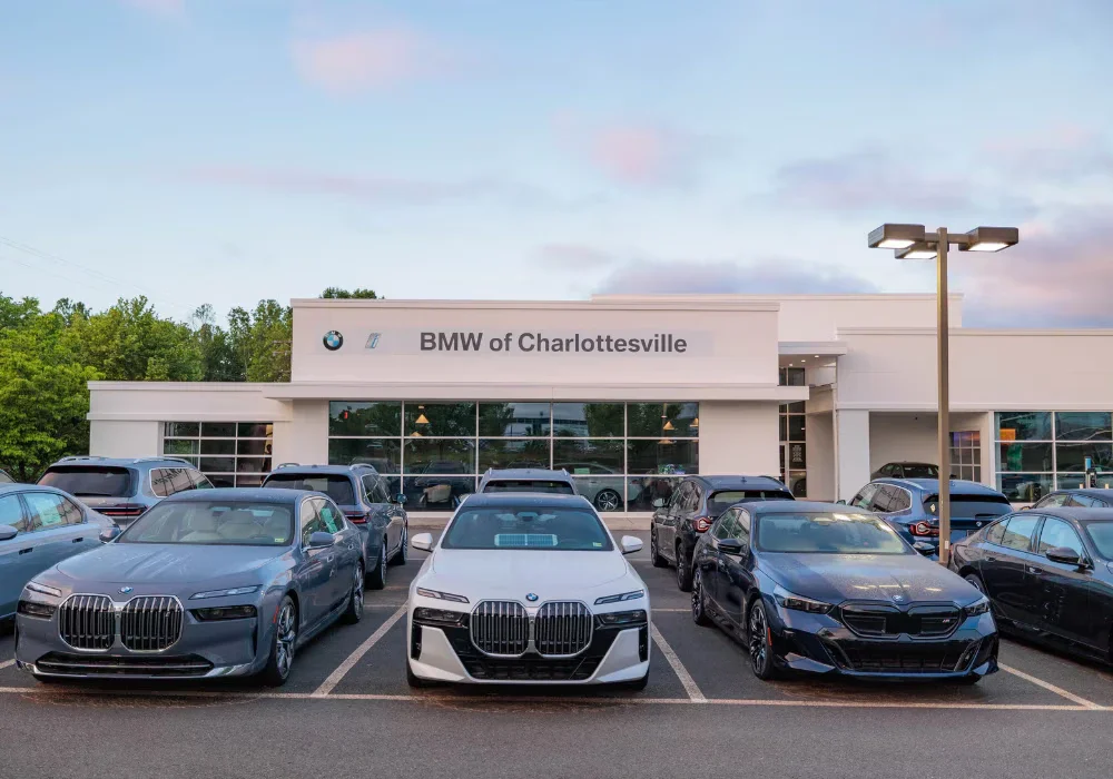 BMW of Charlottesville dealership building with rows of new BMW cars parked in front under a cloudy sky.