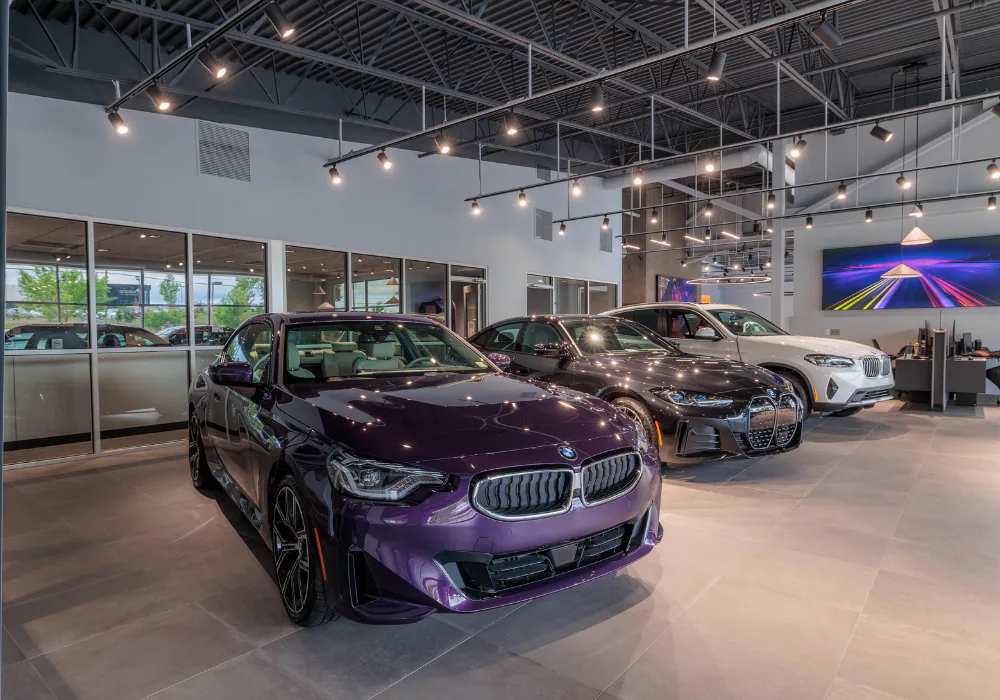 Purple coupe, dark sedan, and white SUV displayed on a bright showroom floor with large windows and modern lighting.